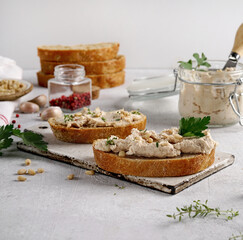 Homemade pate, spread or mousse in glass jar with sliced bread and herbs, light concrete background.