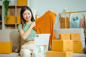 young Asian entrepreneur, the owner of a small clothing store, organizes online live streams showcasing products packaged in cardboard boxes, ensuring prompt and efficient delivery.