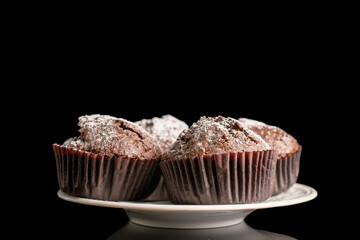 Four chocolate muffins on a white ceramic saucer, macro, isolated on a black background.