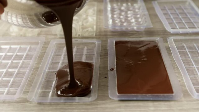 A chocolatier pours chocolate into plastic molds. Production of craft sweets.