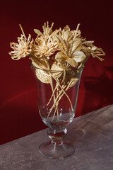 A glass vase with a bouquet of flowers made from straw on a red background. Straw weaving