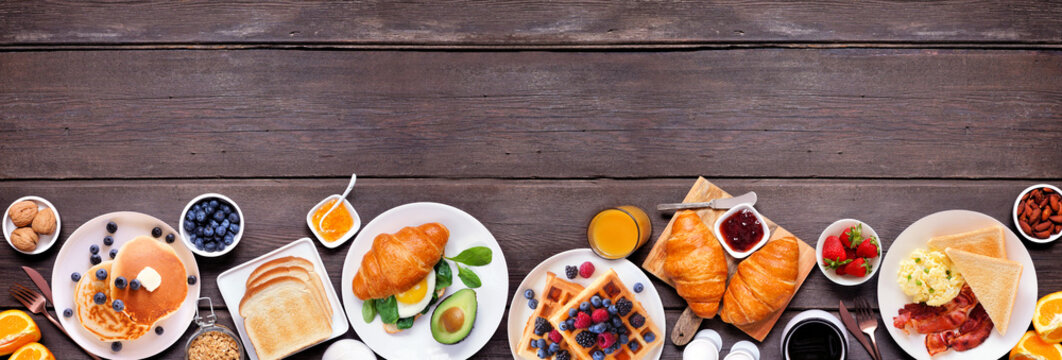 Breakfast or brunch bottom border on a dark wood banner background. Top down view. Assorted sweet and savory food items.