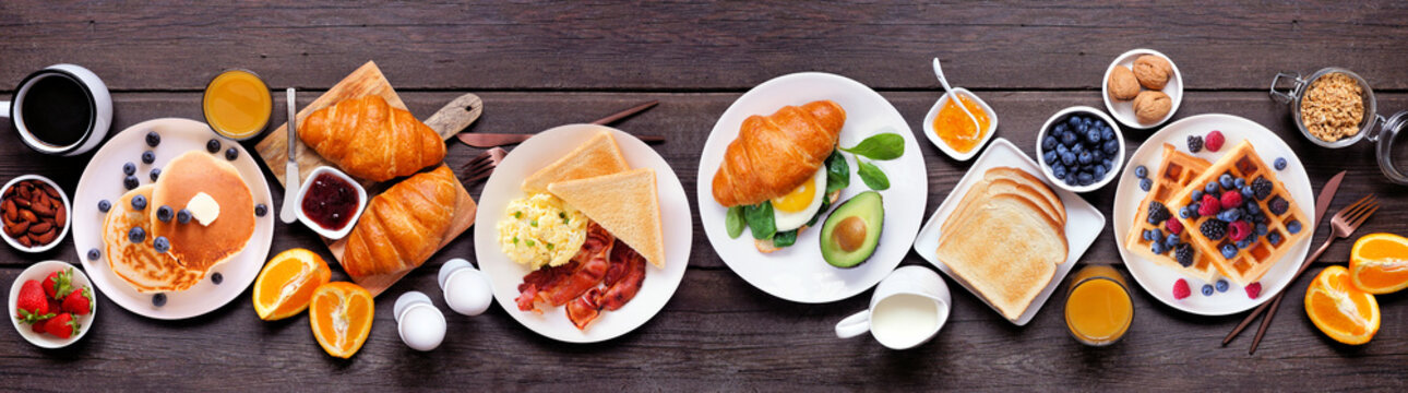 Breakfast or brunch table scene on a dark wood banner background. Top view. Assortment of sweet and savory food items.