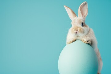 Obraz premium Easter Bunny holding a large Easter egg in pastel blue background, copy space.