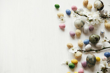 Easter flat lay. Stylish easter eggs and cherry blossom on rustic white table. Happy Easter! Easter border with space for text. Modern dye marble and colorful chocolate eggs and spring flowers