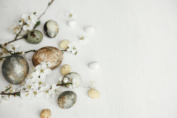 Stylish easter eggs and cherry blossom on rustic white table. Happy Easter! Minimal easter border template with space for text. Modern natural dye marble eggs and spring flowers
