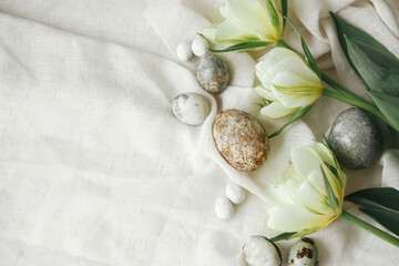 Stylish easter eggs and tulips on rustic table with linen cloth. Happy Easter! Easter flat lay. Modern natural dye marble eggs and spring flowers, holiday banner