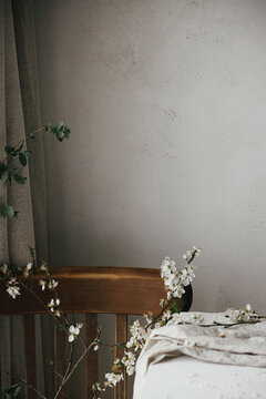 Beautiful cherry branch on linen cloth on rustic white table and old wooden chair composition. Spring countryside still life. White cherry blossom, rural flowers banner