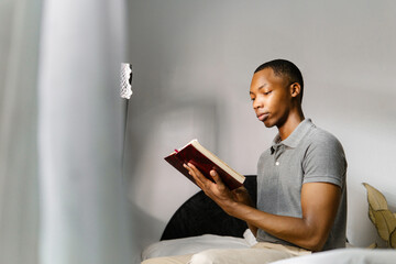 Man in gray shirt reading a book at home.