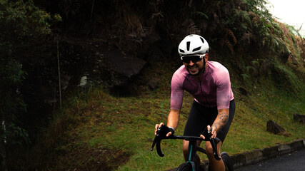 Cyclist man making an effort and painfull face in pink cycling jersey who is riding on road bike in...