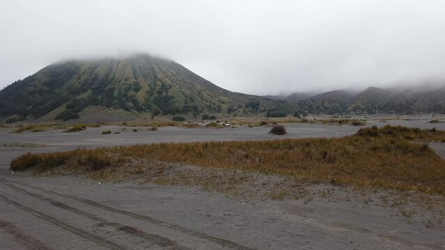 Tourist vehicle driving through the area called "sea of sand"  around Mount Bromo. Mount Batok caldera visible in the background