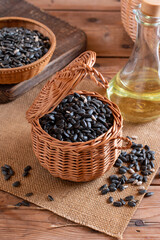 Black sunflower seeds in small brown wooden cup, on wooden table