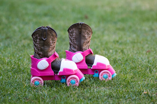 A little girl's pink plastic roller skates were left on the green lawn with her cowboy boots still in the roller skates.
