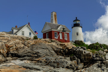 Fototapeta na wymiar Pemaquid Point Lighthouse and Bell Tower in Bristol Maine sits atop rugged rock layers on a bright summer day dotted with puffy clouds