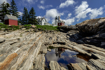 Pemaquid Point Lighthouse and Bell Tower in Bristol Maine reflection in puddle on a bright summer day dotted with puffy clouds