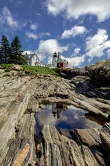 Pemaquid Point Lighthouse and Bell Tower in Bristol Maine reflection in puddle on a bright summer day dotted with puffy clouds