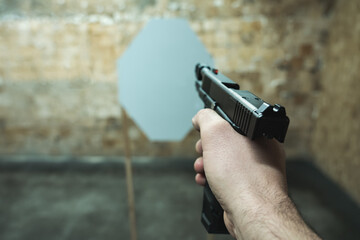 A pistol in a man's hand is aimed at a paper target at a shooting range.