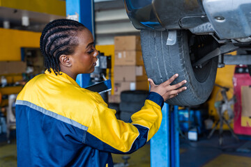 Black car mechanic woman checking tire in tire shop and auto repair garage
