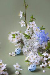White  blossom branches in a glass vase , easter eggs, pastel green  background. Small beautiful bouquet of the cherry flowers. Vintage  easter template, spring greeting card.