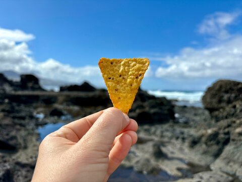 A piece of flavored tortilla chips in hand isolated close up on a summer sea background in Tenerife, Canary Islands, Spain