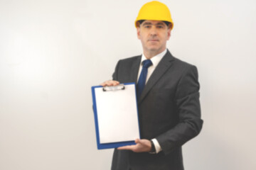 A man in a helmet holds a folder with a white sheet in his hands. A man  holding a folder over isolated background, blurry photo