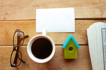 Newspaper, toy house, coffee cup and glasses on wooden background. Quarantine concept