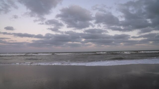 Vacations. Panorama view of the empty beach at sunset. View of the sandy shore and ocean weaves under a beautiful sky with dusk colors. 