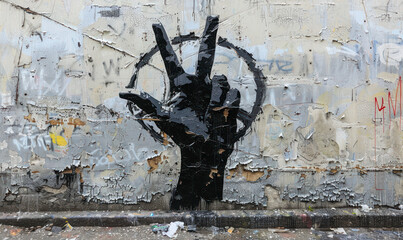 Street art of a black painted hand making a peace sign against a weathered white wall, representing...