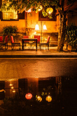 A table set up for patrons at a restaurant in Hoi An, Vietnam waits for customers with the oarange glow of the city lights illuminating the street.