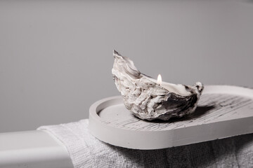 A candle in the oyster shell burning. Light stand on the bath cloth.