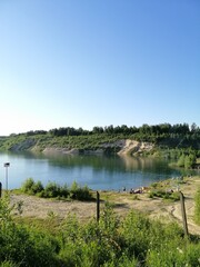 a dug sand quarry with a lake and people resting on the sand on a sunny day. Nature wallpaper