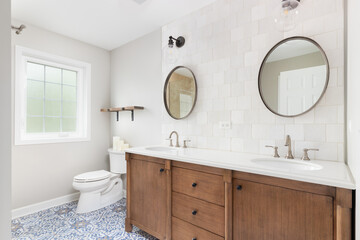 A bathroom with a brown tiled wall with lights mounted over circular mirrors, natural wood cabinet, and a blue and white mosaic tile floor. No brands or labels.