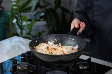 Close up of Chef cook hands cooking roasted vegetables with rice for Asian cuisine in frying wok pan on gas stove.