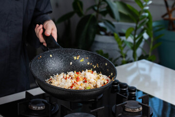 Close up of Chef cook hands cooking roasted vegetables with rice for Asian cuisine in frying wok pan on gas stove.