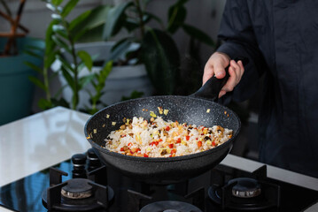 Close up of Chef cook hands cooking roasted vegetables with rice for Asian cuisine in frying wok pan on gas stove.