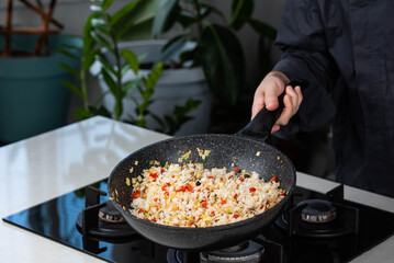 Close up of Chef cook hands cooking roasted vegetables with rice for Asian cuisine in frying wok pan on gas stove.