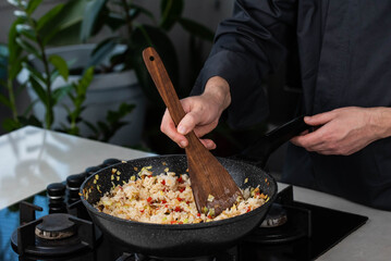 Close up of Chef cook hands cooking roasted vegetables with rice for Asian cuisine in frying wok pan on gas stove.
