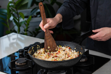 Close up of Chef cook hands cooking roasted vegetables with rice for Asian cuisine in frying wok pan on gas stove.