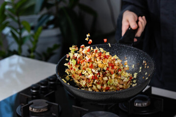 Close up of Chef cook hands cooking and toss roasted onion, pepper, Shiitake mushrooms, cabbage, garlic in frying wok pan on gas stove. Flying food levitation.