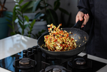 Close up of Chef cook hands cooking and toss roasted onion, pepper, Shiitake mushrooms, cabbage, garlic in frying wok pan on gas stove. Flying food levitation.