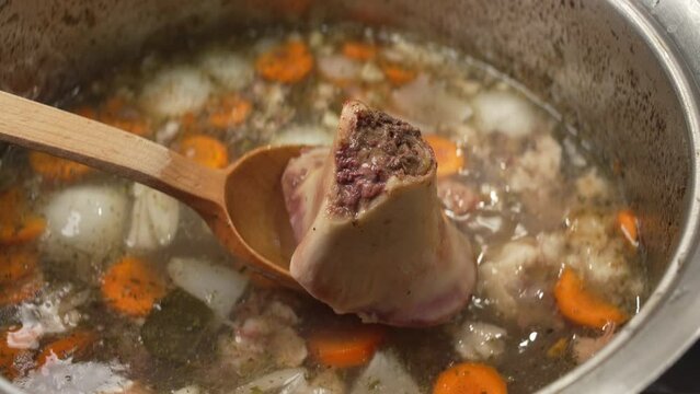 Stir with a wooden spoon delicious bone broth with carrots and spices and internal structure of chopped bone