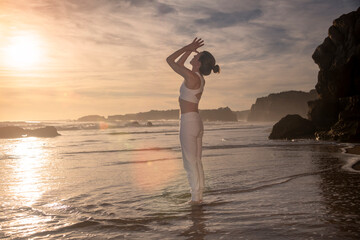 woman standing on a beach meditating at sunrise, sunset