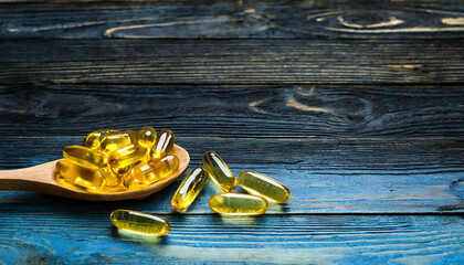 Cod liver oil omega 3 gel capsules in a wooden spoon  on vintage grunge background
