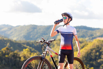 Brazilian cyclist enjoying a break atop a mountain, hydrating with water while soaking in nature's tranquility. Ideal for those seeking a healthy lifestyle with outdoor exercise