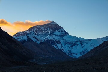 Fototapeta premium Experience the breathtaking spectacle of sunrise over Mt. Everest as its towering silhouette casts a majestic shadow against the dawn-lit sky, while vibrant crimson hues dance atop the veiling clouds.