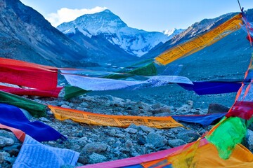 Mt. Everest towers in the distance while colorful Tibetan prayer flags sway in the foreground,...