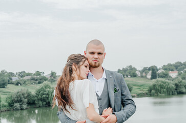 the bride and groom embrace on the background of the lake