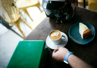 A motorcyclist's helmet and a cup of coffee on a table. Patterned coffee