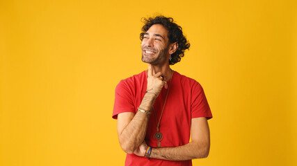 Pensive attractive man with curly hair, dressed in red T-shirt,  thinking something, having good...