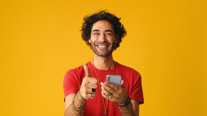 Man with curly hair wearing red T-shirt, using mobile phone gives thumbs up hold in hand do online...